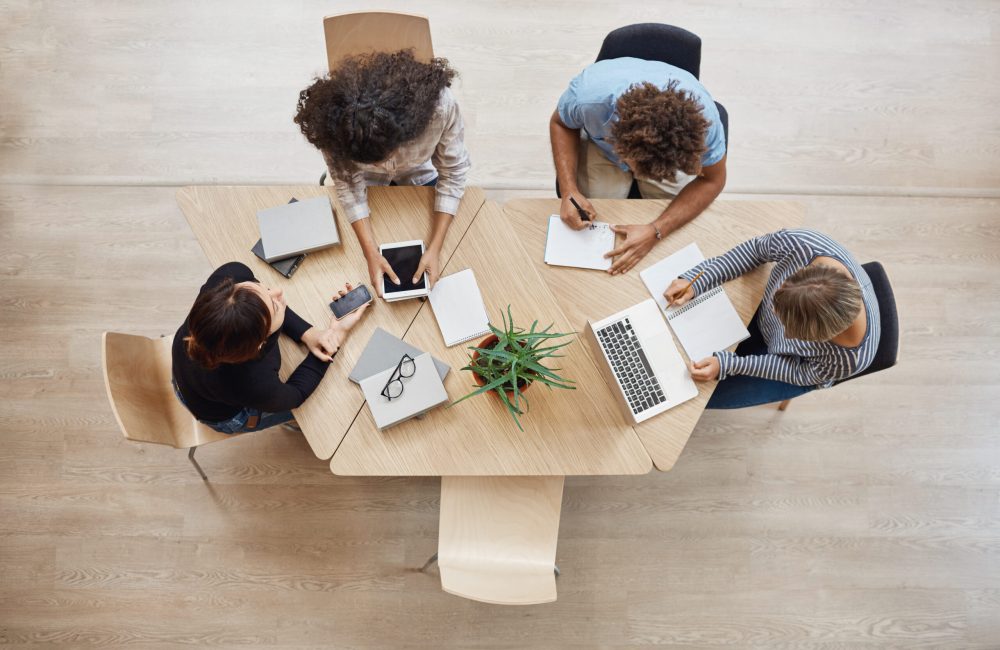 View from above. Business,startup, teamwork concept. Startup partners sitting at coworking space talking about future project, looking through examples of work on laptop and digital tablet